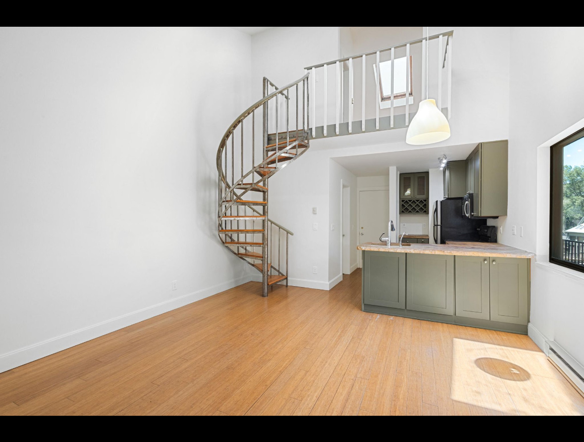 Sculptural metal spiral staircase rising from the living room to the upstairs bedroom under a skylight